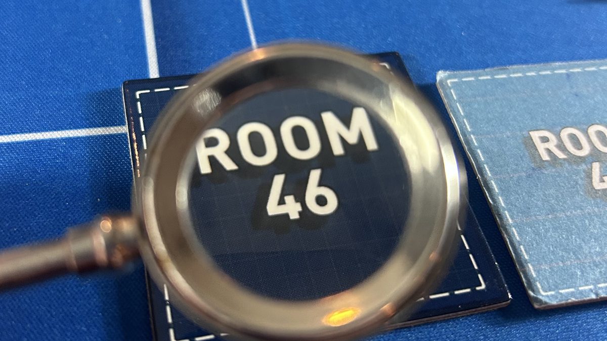 A magnifying glass held over a tile reading Room 46