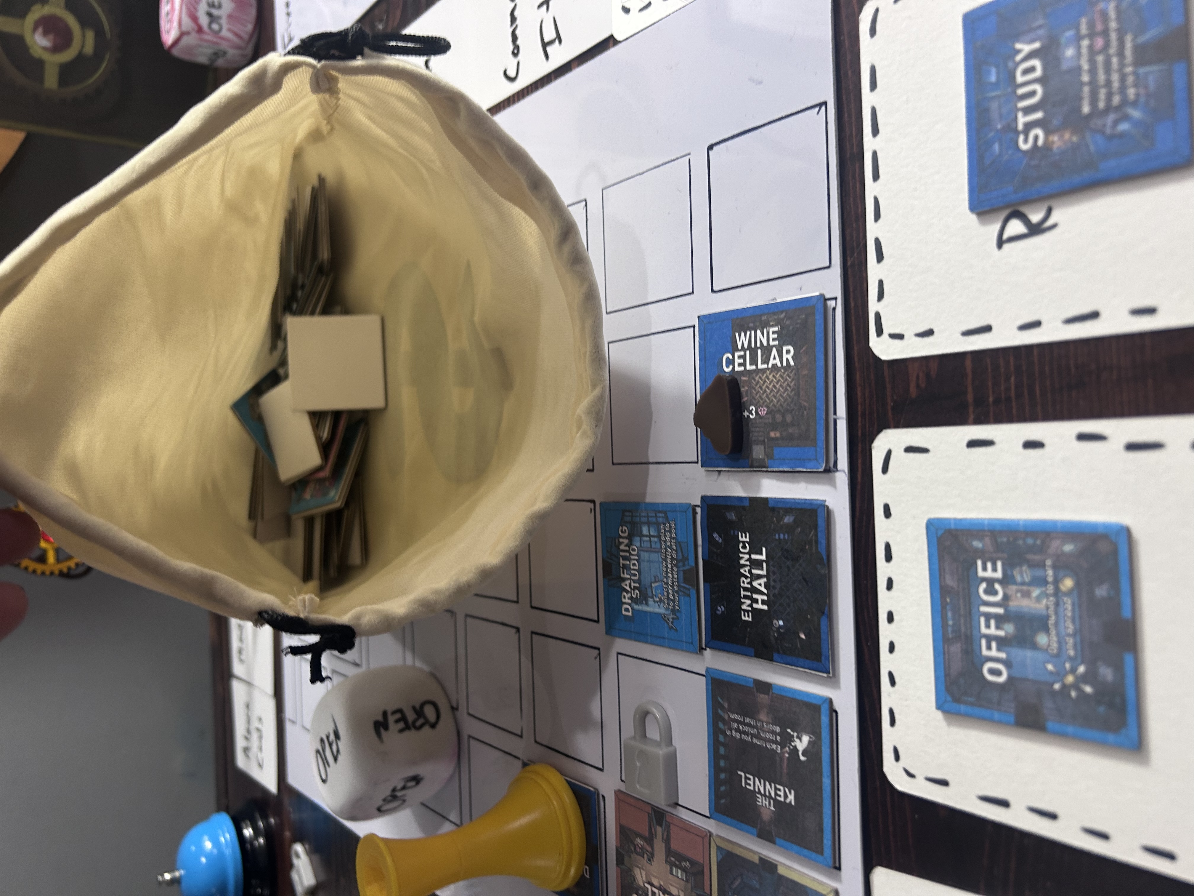 The drawstring bag held open over the board, tiles visible inside, OPEN die and Entrance Hall on the grid below