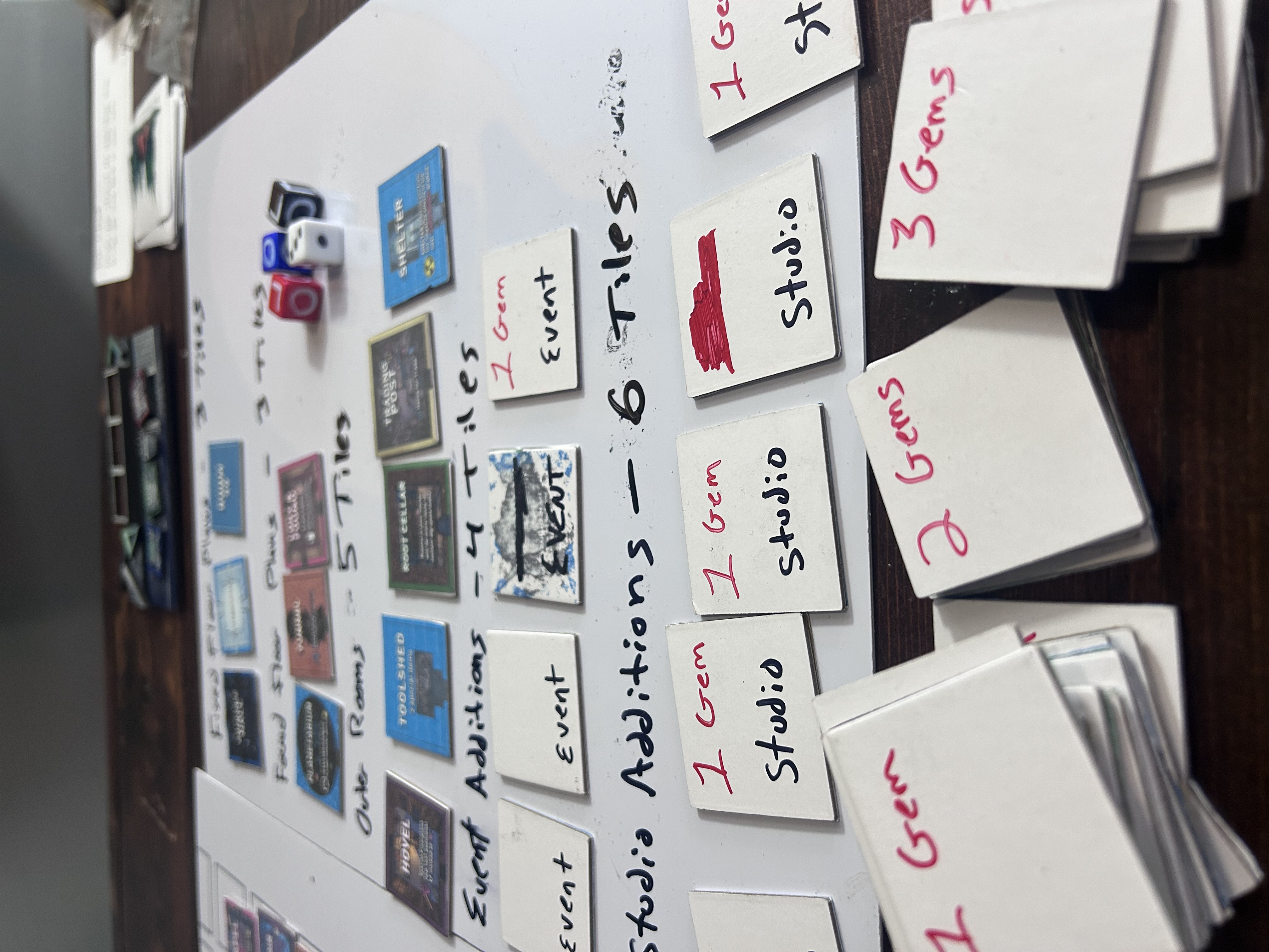 Prototype tile backs with scribbled-out old values and new costs written over in red Sharpie