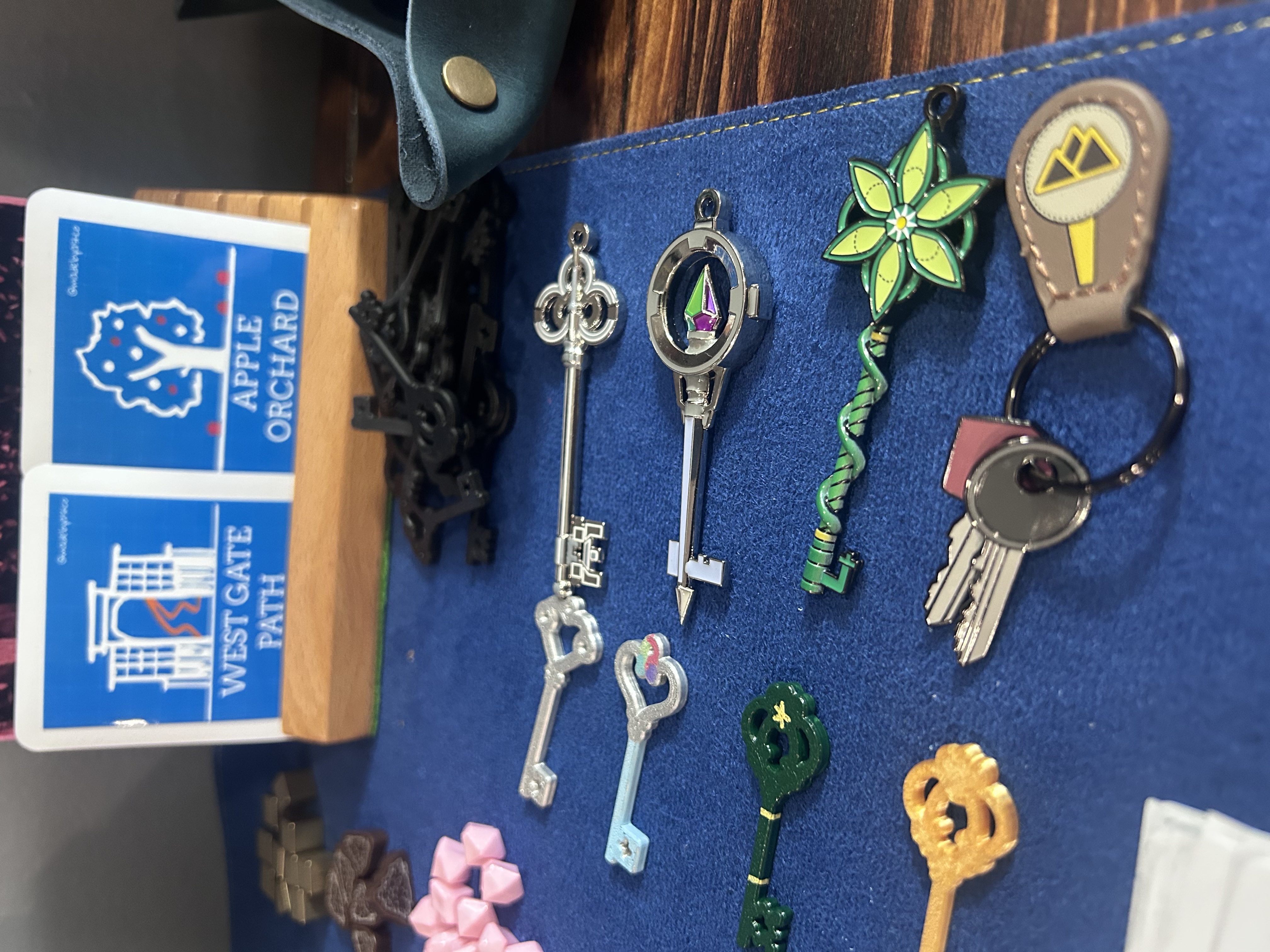 Collection of decorative physical special keys spread across the navy mat — ornate silver keys, a green flower key, a compass key, a rainbow crystal key, and others, with Manor cards and lock tokens in background