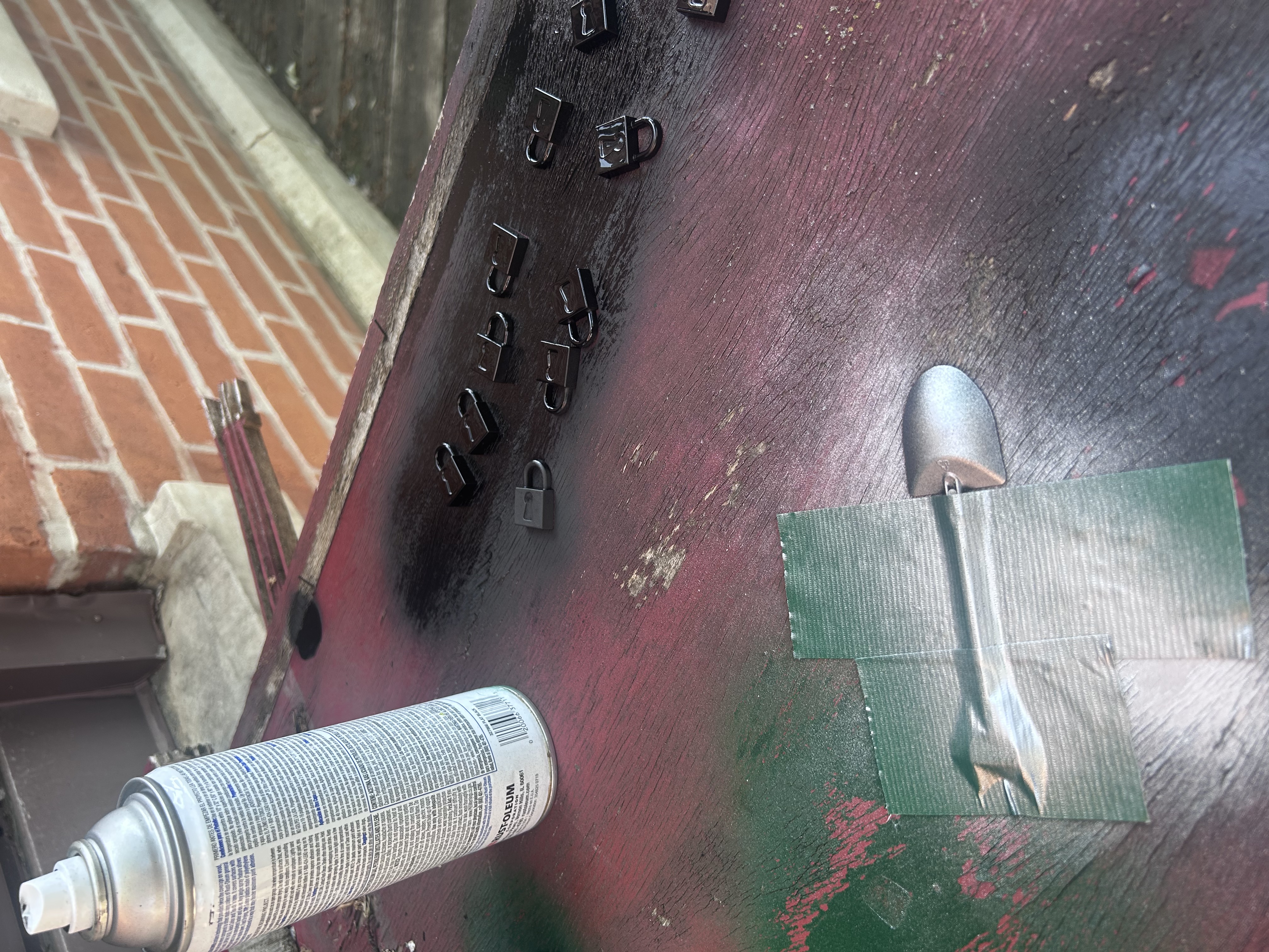 Padlock tokens and shovel being spray painted black and gray on a workbench outside