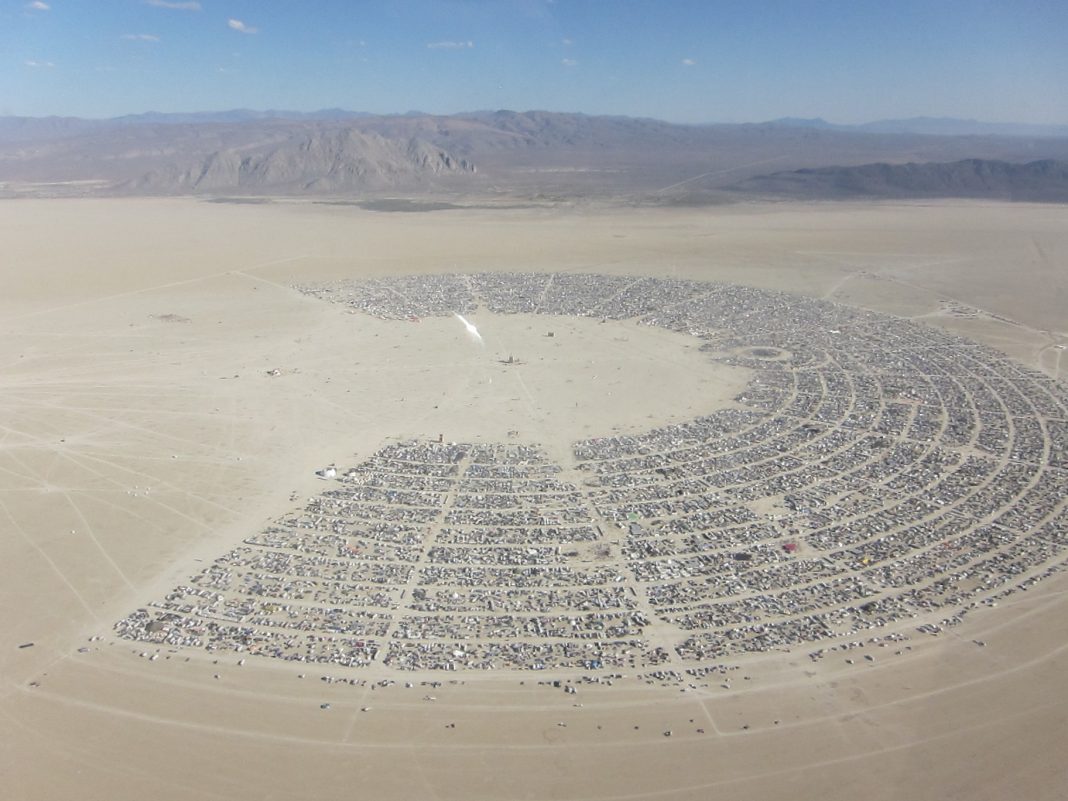 Full aerial view of Black Rock City — the entire playa layout visible from above, organized around a distant center point