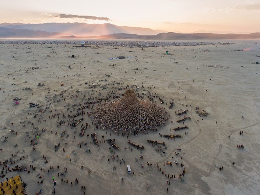 Aerial view of a latticed wooden temple structure at Burning Man surrounded by crowds at sunset on the playa