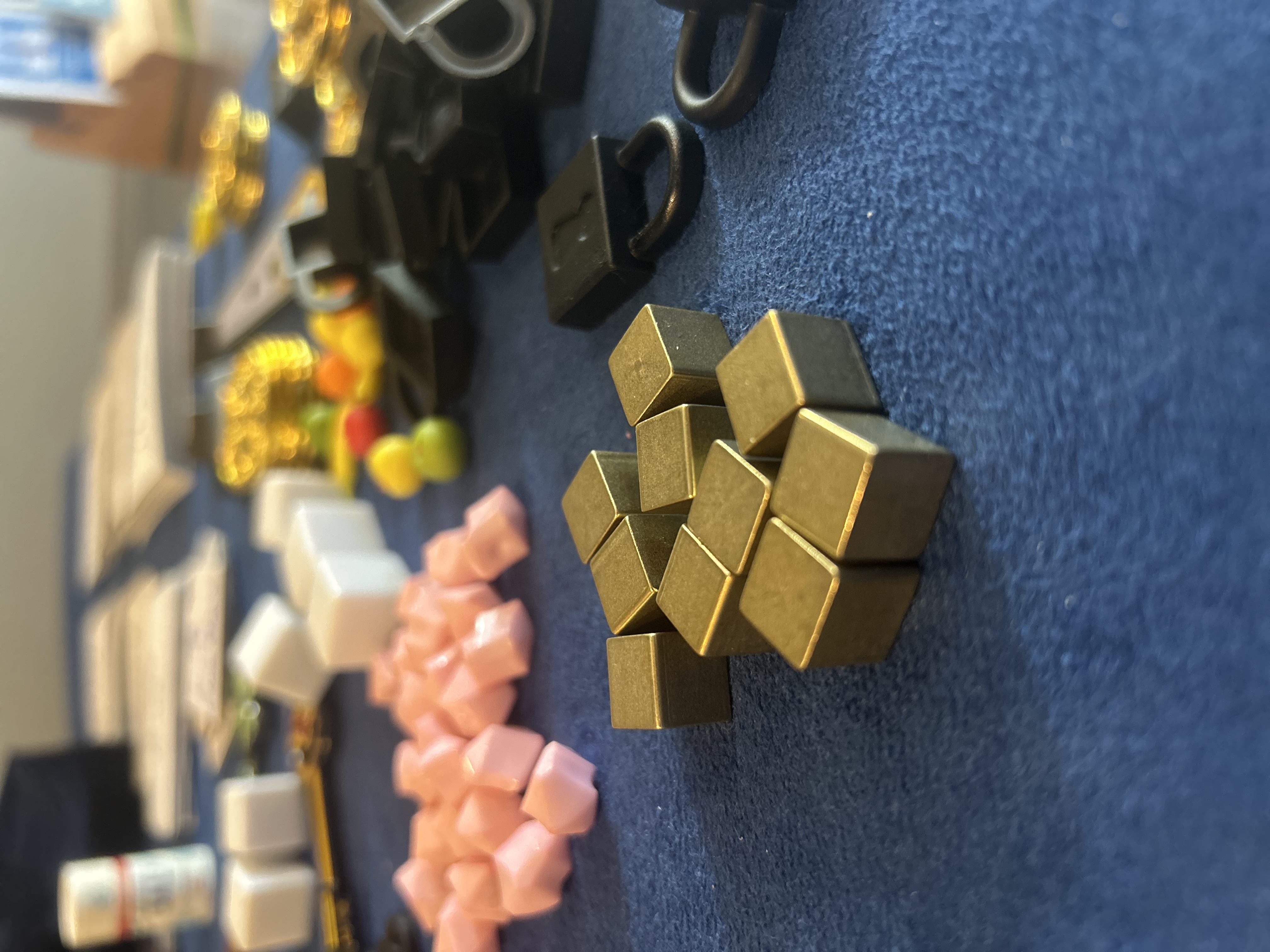 Ten small brass metal cubes clustered together on the blue mat, with gems and padlocks blurred in the background