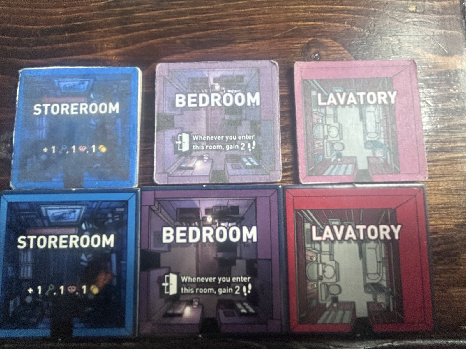 Two rows of three tiles — Storeroom, Bedroom, Lavatory. Top row: the small, faded, worn first-prototype tiles. Bottom row: the produced tiles, larger, saturated, sharp-edged