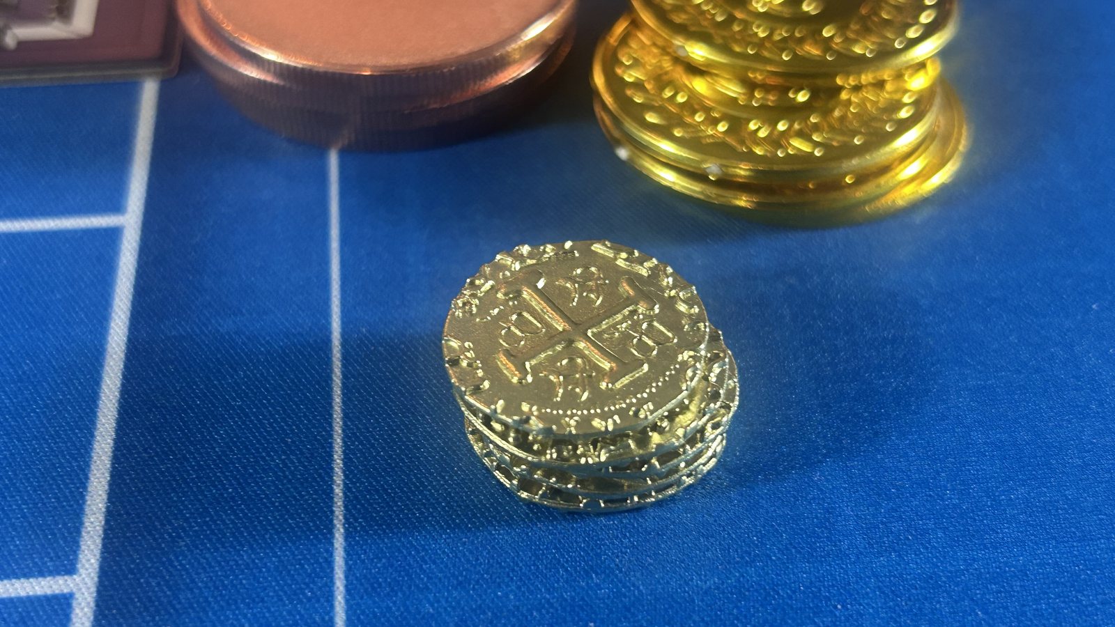 A large flat copper placeholder coin beside a stack of small embossed gold doubloons