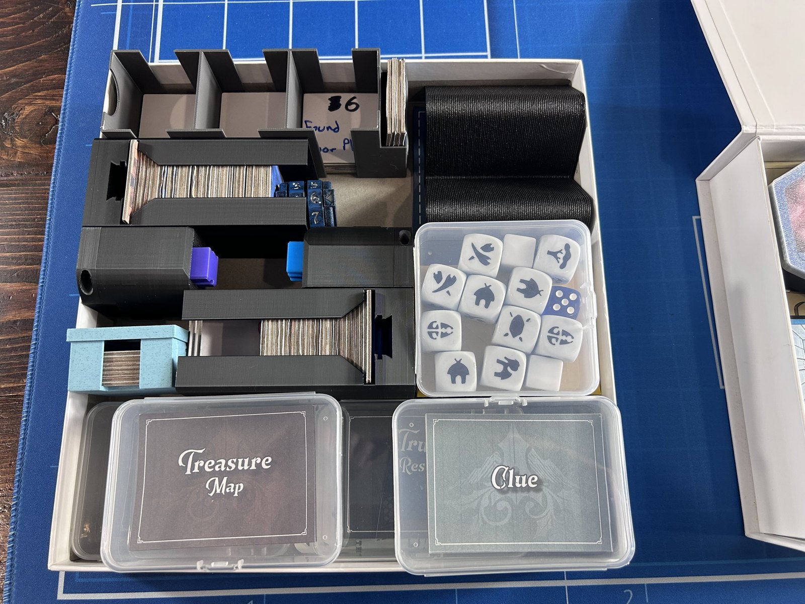 The game box insert, packed: stacks of room tiles in slots, four card decks in cases, a box of constellation dice, rank markers, and a handwritten label reading Found Floor Plans