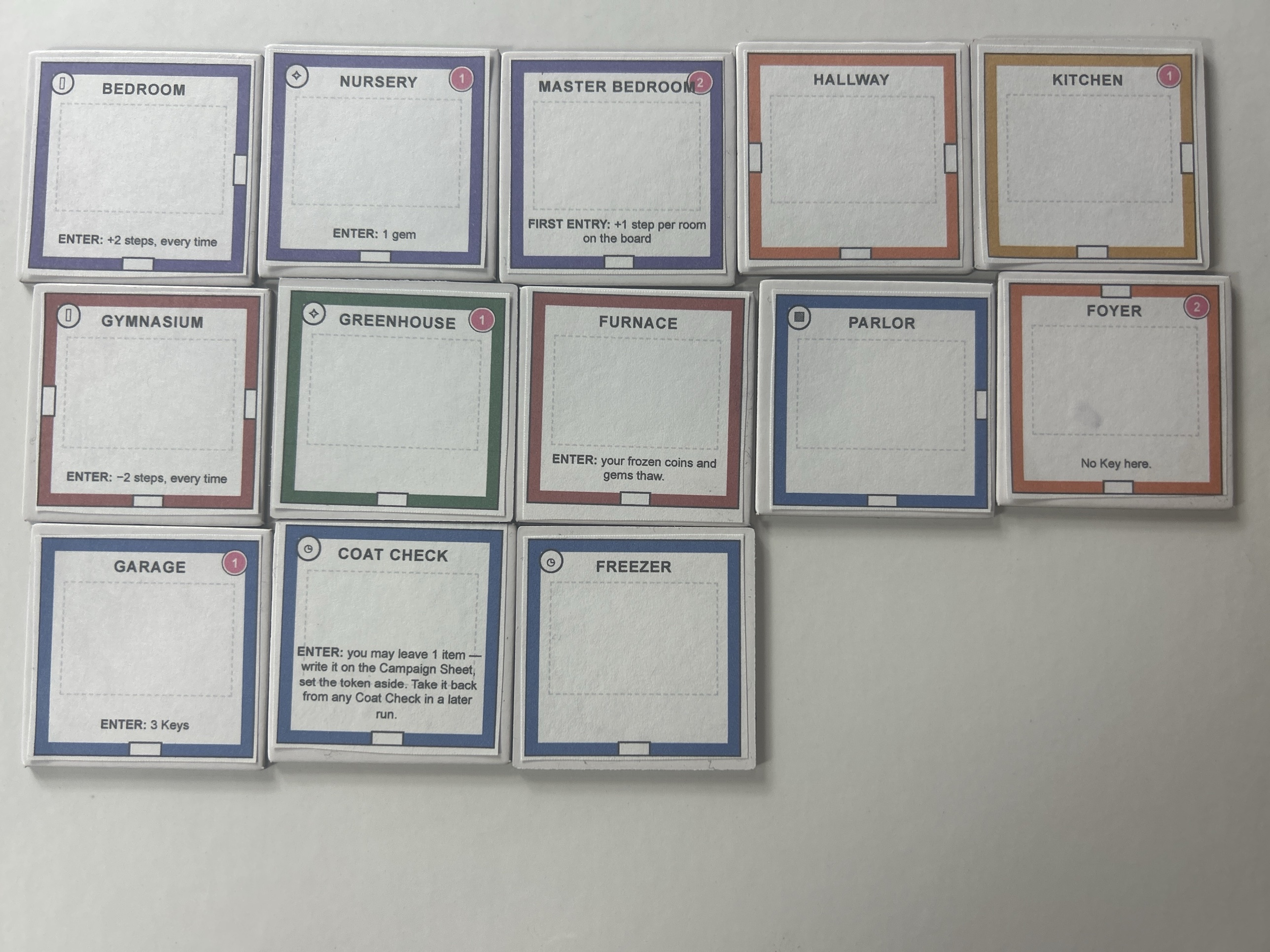 Thirteen printed and mounted room tile fronts laid out on a white surface, each with a coloured border, room name, gem cost and one line of rule text &mdash; Bedroom, Nursery, Master Bedroom, Hallway, Kitchen, Gymnasium, Greenhouse, Furnace, Parlor, Foyer, Garage, Coat Check and Freezer