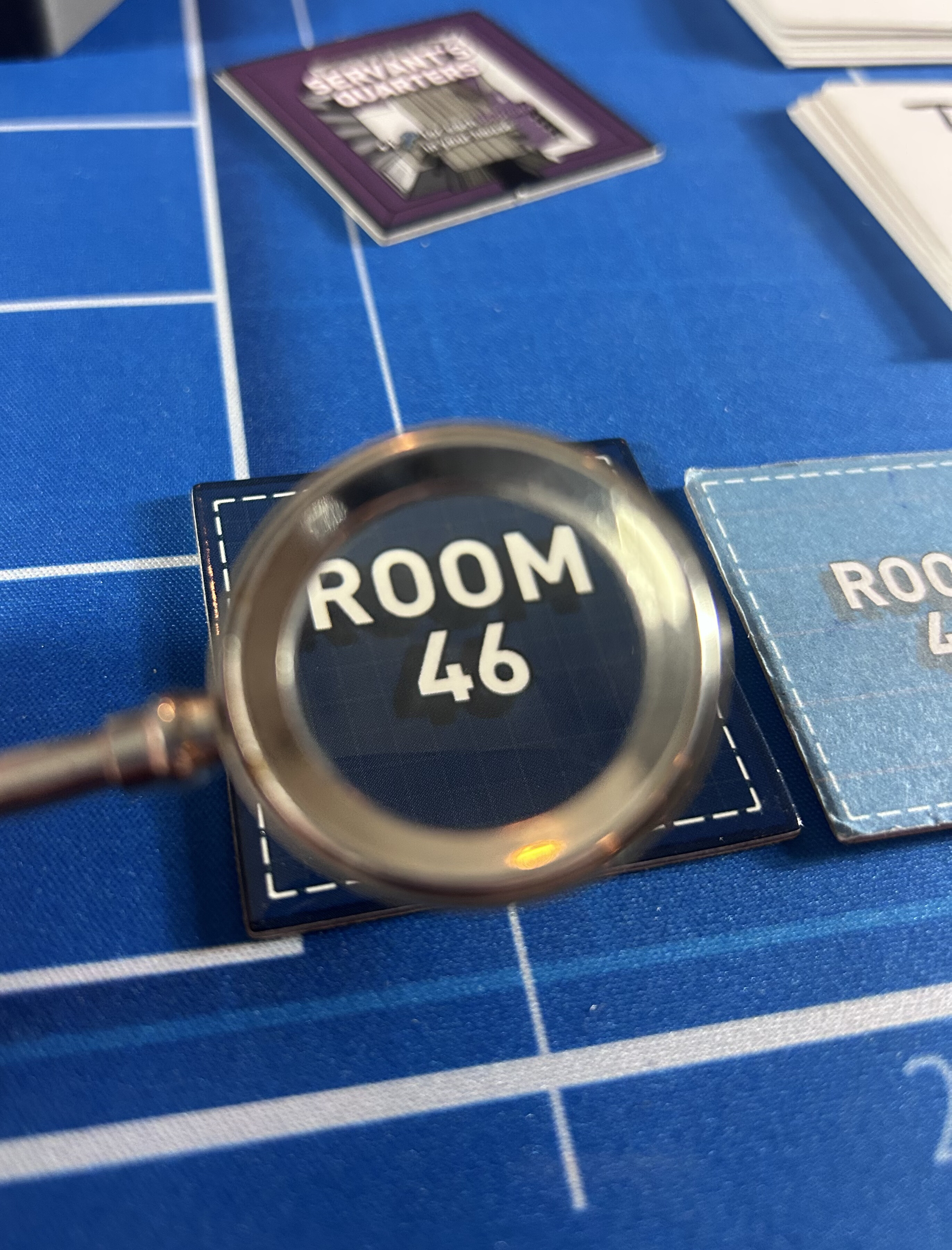 A magnifying glass held over a tile reading Room 46 on the blue Mount Holly Estate board