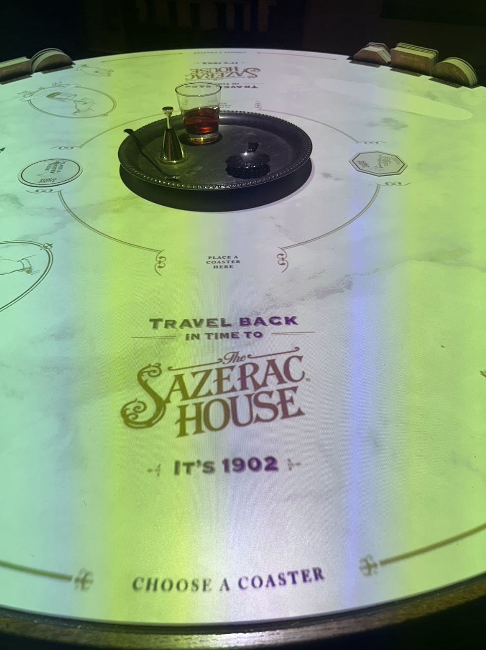 The interactive Sazerac House table — coasters arranged in a circle, projected display, a drink at center